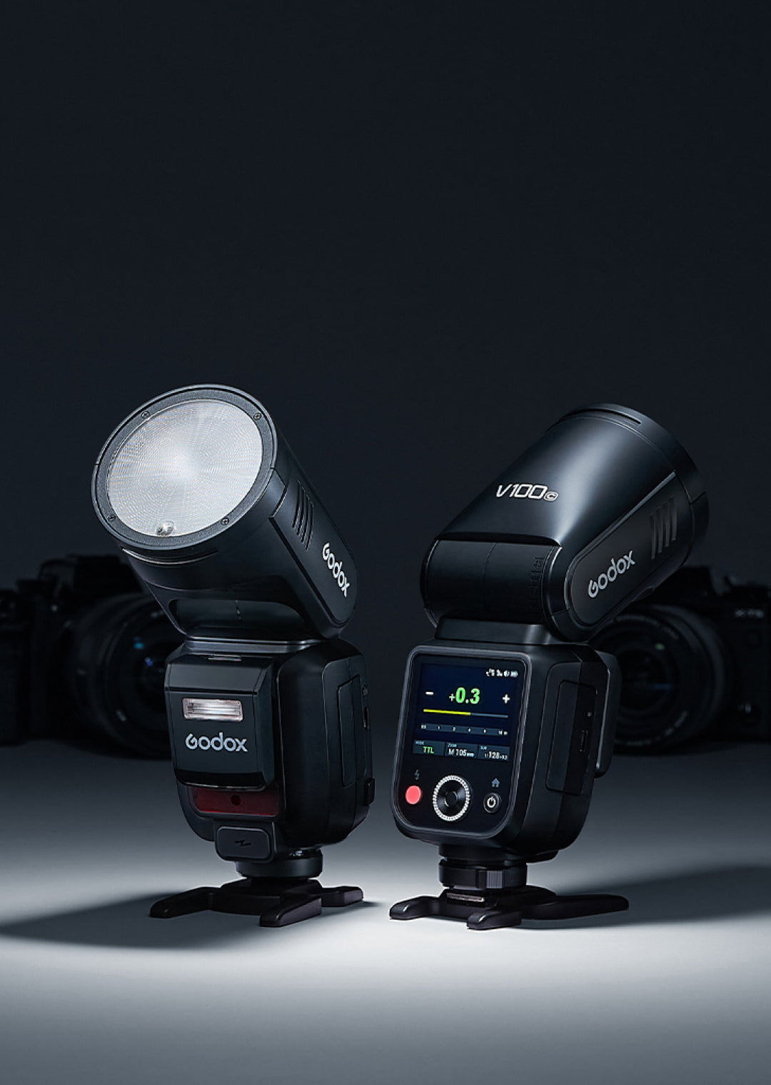 Godox V100 A black Godox V100 camera flash with a round head is centered against a dark grey background. The Godox logo is visible in orange at the top, and in white on the lower body of the flash. Text above the flash reads