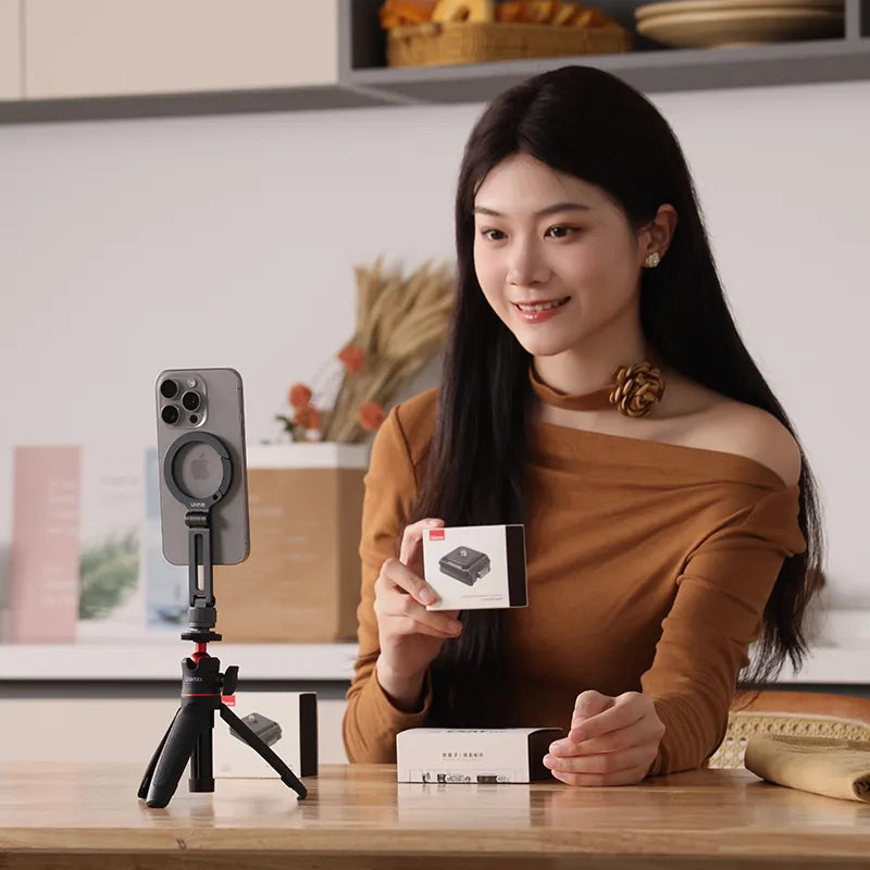 Woman holding a product box with a smartphone on a tripod in a kitchen setting