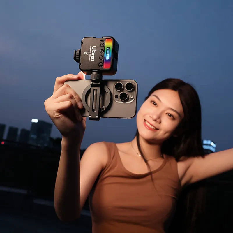 Woman holding a smartphone with a camera attachment against a city skyline at night.