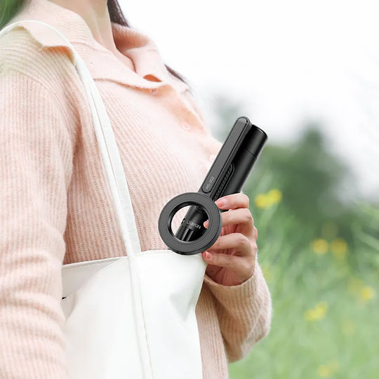 Person holding a black Ulanzi MG-002 Magnetic Tripod/Selfie Stick against a blurred natural background