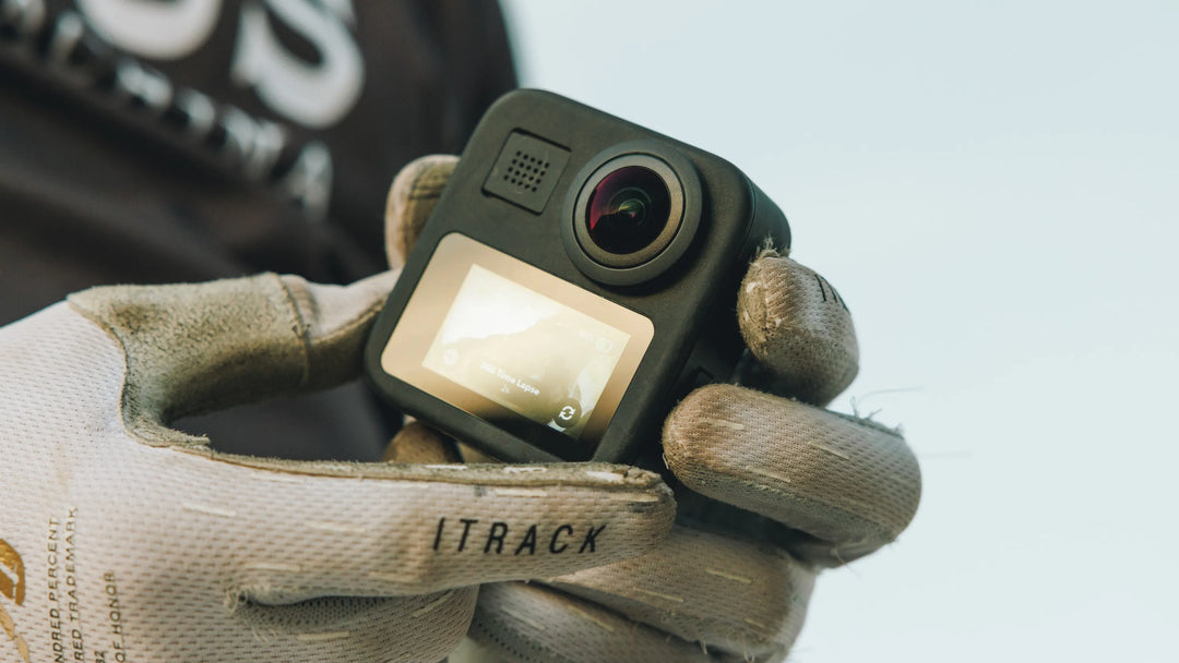 Hand wearing a rugged glove holding a small camera labeled 'ITRACK' against a blurred background.