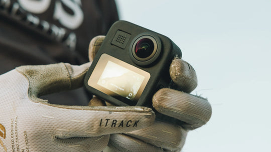 Hand wearing a rugged glove holding a small camera labeled 'ITRACK' against a blurred background.