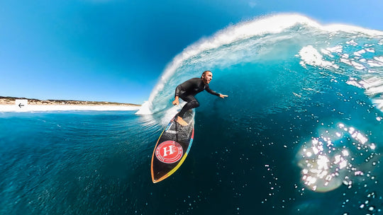 Surfer riding a wave with a clear blue sky and ocean.