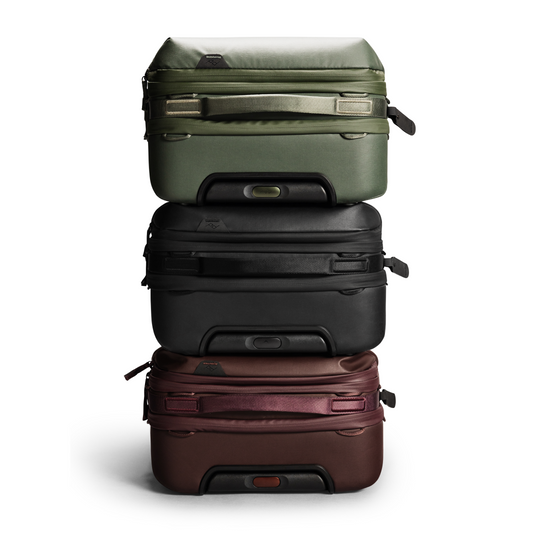 Stack of three suitcases in green, black, and brown on a white background