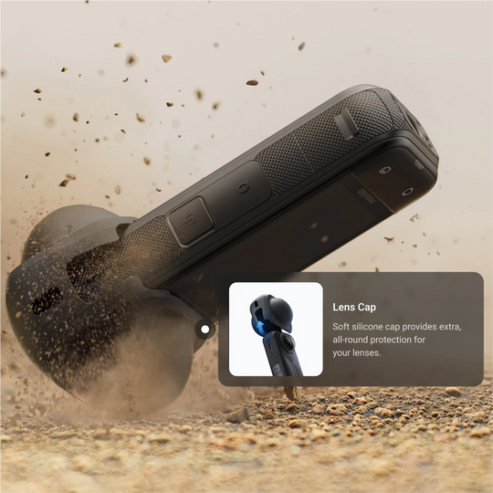 Black camera with lens cap feature being hit by a rock on a sandy background