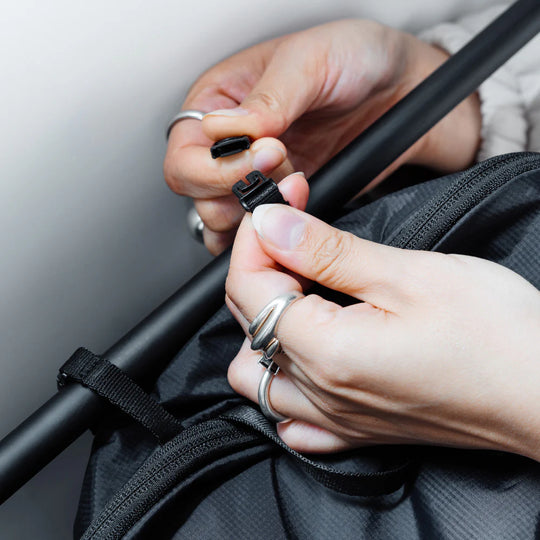 Close-up of hands securing a black strap on a bag against a neutral background