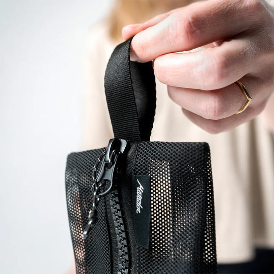 Person holding a black mesh pouch with a zipper, featuring the brand 'Matador'.