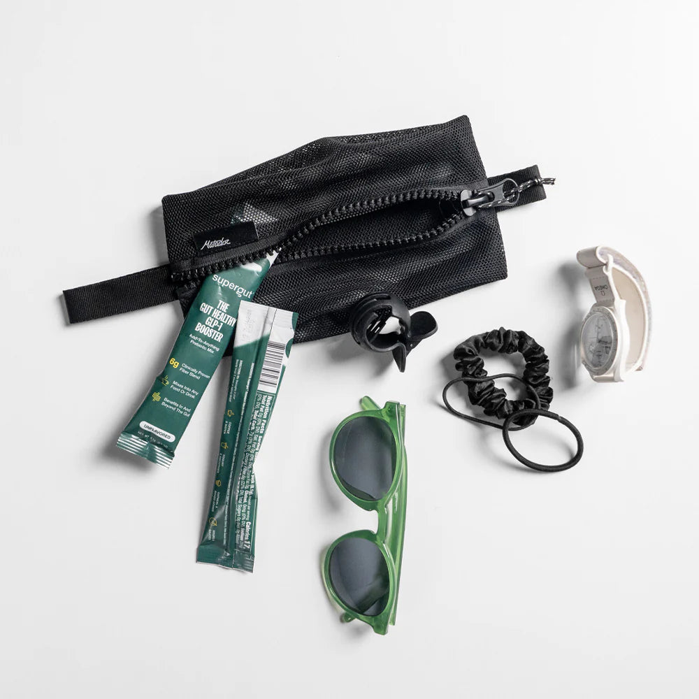 Black zippered pouch, green sunglasses, and other accessories on a white background
