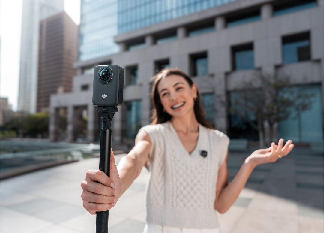 Woman holding a camera on a selfie stick with a cityscape background