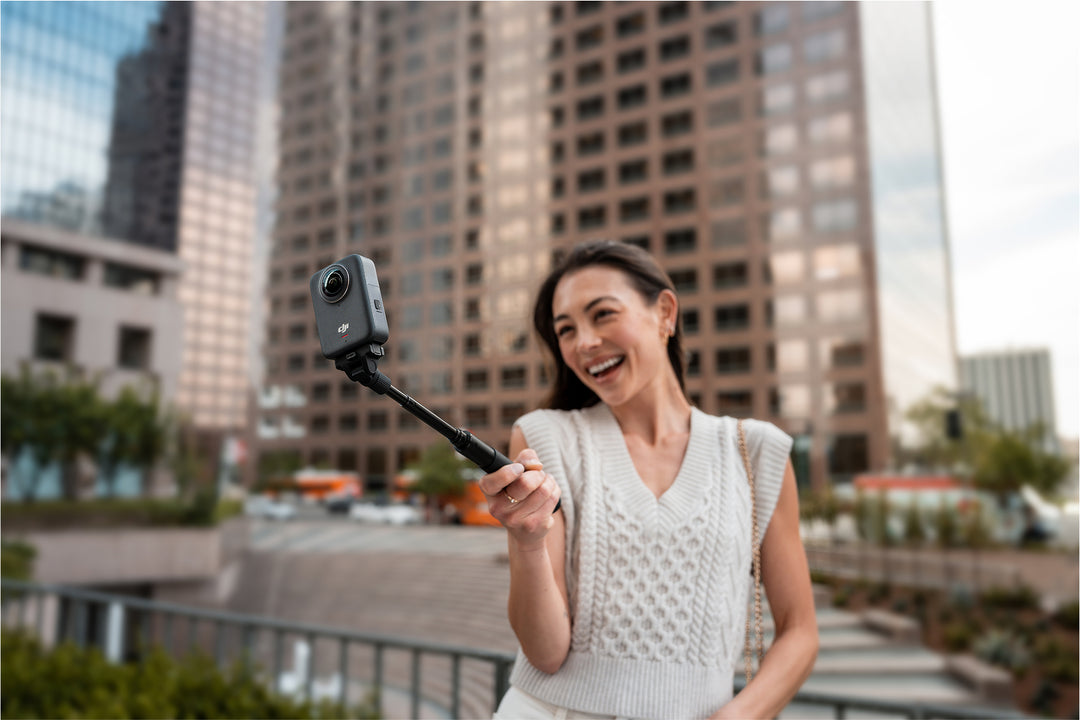 Woman holding a camera on a selfie stick with a cityscape background