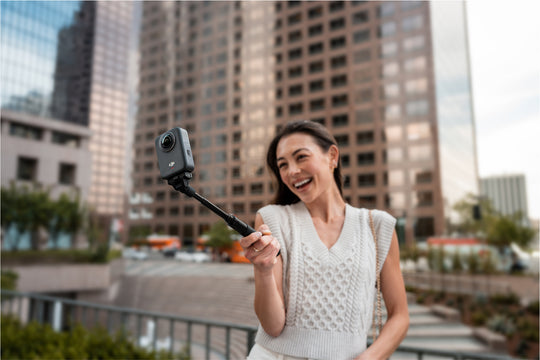 Woman holding a camera on a selfie stick with a cityscape background