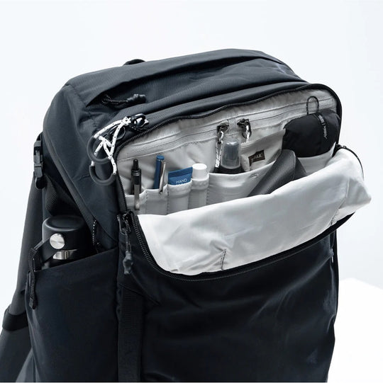 A black travel backpack with the top zipper open, showing organized compartments filled with travel-sized items like bottles and pouches.