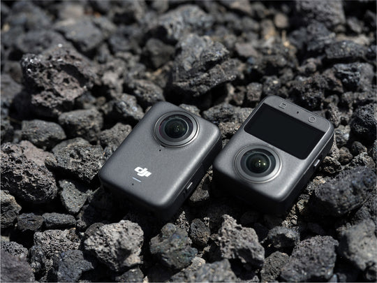 Two cameras on a bed of dark gray stones