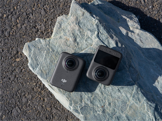 Two black action cameras on a stone surface with a natural outdoor background
