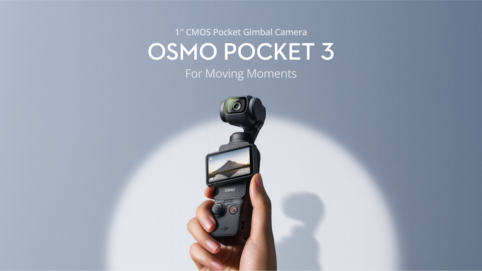 A hand holds up a black DJI Osmo Pocket 3 gimbal camera against a light grey background. The camera's screen displays a landscape with a mountain. The text 